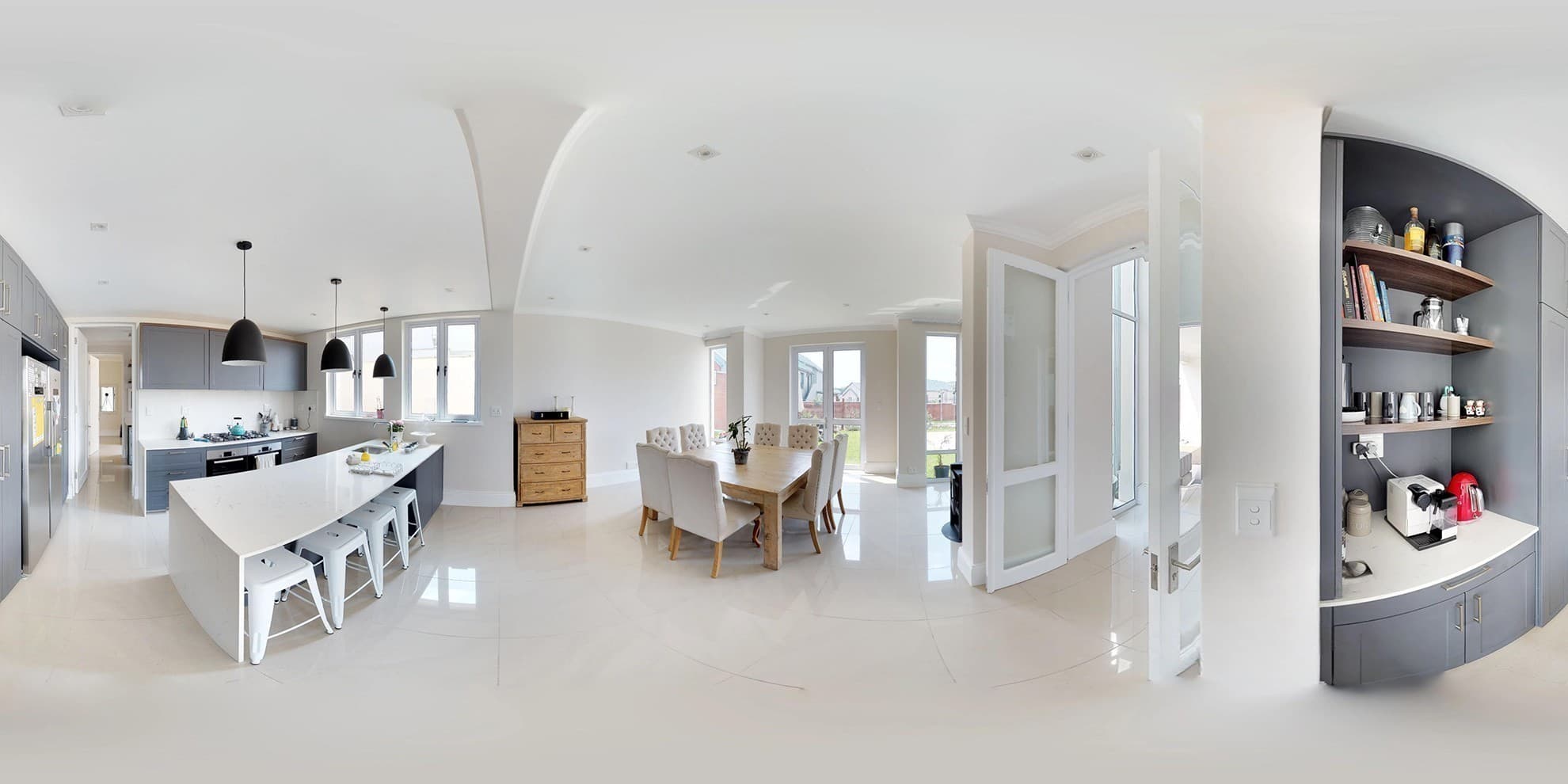 A panoramic view across a bright kitchen and living area