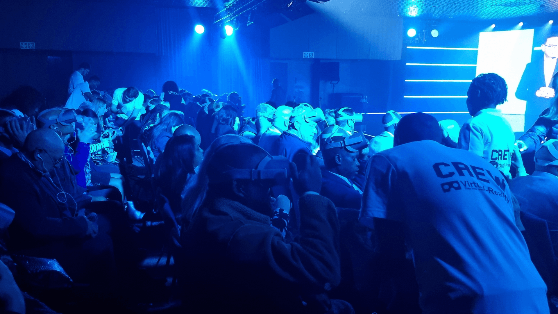 An audience participating in a VR experience at an event with blue stage lighting