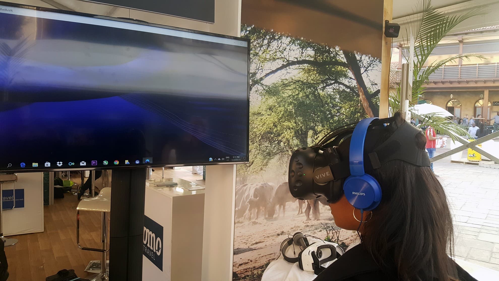 A guest wearing a VR headset and headphones at a station with a TV screen