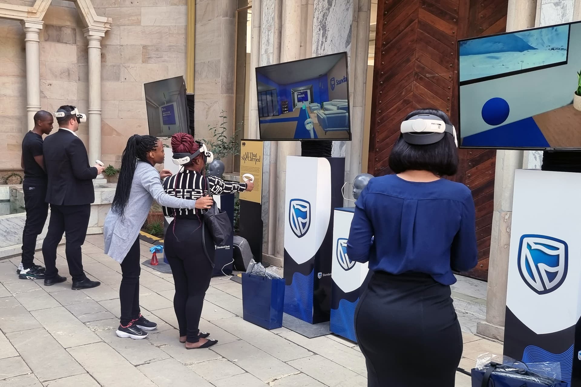 Guests using VR headsets at Standard Bank event stations with TV screens